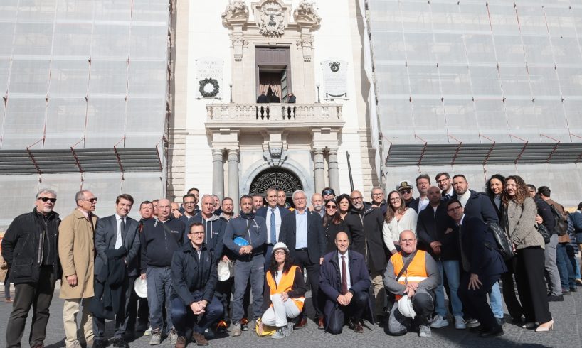È stata svelata in piazza Duomo a Catania il prospetto restaurato della facciata centrale di Palazzo degli Elefanti, riportando alla luce il volto autentico dell'edificio simbolo della città. L'intervento di tutela e riqualificazione, avviato nel giugno dello scorso anno, è stato finanziato dalla Regione Siciliana e progettato dalla direzione Lavori pubblici comunale. Il sindaco Enrico Trantino ha sottolineato come il `volto´ del Municipio sia il risultato di una ricostruzione filologica condotta in coerenza con le indicazioni della Soprintendenza, evidenziando il ruolo decisivo della ricomposizione cromatica della facciata. Le prove preliminari di pulitura hanno infatti rivelato l'originaria dialettica tra la tonalità giallo sabbia degli intonaci e il candore della pietra calcarea, elementi che nel progetto settecentesco definivano l'equilibrio prospettico del Palazzo degli Eelefanti. Grazie a leggere velature di pigmenti naturali e al ripristino delle finiture originarie, il prospetto riacquista oggi la brillantezza perduta, mettendo in evidenza il ritmo dei pilastri, dei timpani e del grande balcone centrale retto dalle colonne in granito. L'effetto restituito alla piazza richiama l'antica scena urbana immaginata da Vaccarini, in cui la facciata del municipio torna a dialogare con la Cattedrale, il Seminario dei Chierici e il monumento al Liotru, riportando le cromie che per secoli hanno caratterizzato il cuore barocco della città e restituendo ai catanesi un'immagine nitida e fedele del loro palazzo civico. Il restauro ha riguardato soprattutto il consolidamento sismico dell'edificio, cuore istituzionale della città e struttura strategica in caso di emergenza. Costruito nel Settecento sulle rovine della loggia medievale distrutta dal terremoto del 1693, il palazzo chiedeva un intervento urgente finalizzato a preservare la continuità delle murature, spesso indebolite da vuoti interni e discontinuità tipiche dei materiali antichi, affrontato mediante potenti iniezioni di calce fluida resistente per il consolidamento dei paramenti e della copertura in calcestruzzo. Parallelamente al miglioramento strutturale, si è operato sul vasto apparato decorativo, tratto distintivo dell'architettura vaccariniana. Ornamenti e lastre rocciose sedimentate, in parte lesionate o distaccate, sono stati ancorati con barre in vetroresina ad alta aderenza o sostituiti con pietra compatibile con l'originale. Le superfici, offuscate da vecchie tinte e depositi legati al traffico urbano, sono state sottoposte a un accurato ciclo di pulitura che ha rimosso gli strati incoerenti senza intaccare la materia. Sul basamento in pietra lavica si è proceduto con sabbiatura controllata, mentre sulle parti in finta pietra l'integrazione è avvenuta con malte idrauliche pigmentate.
